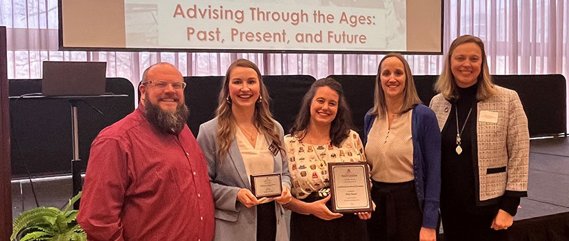 Two advisors are pictured with a man and two women who serve as advising leaders. The advisors are holding an award plaque and smiling at the camera. 