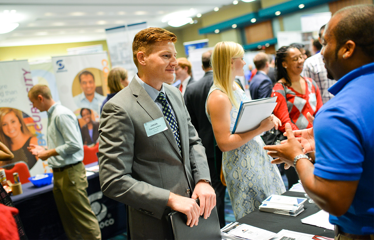 Student in a business suit talks with a recruiter at a career fair.