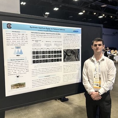 Jack Jeffrey stands in front of his research presentation at the USGIF Symposium