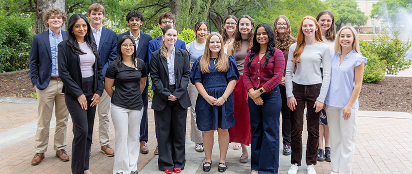 Group of student interns dressed in business casual attire pose together outdoors on campus.