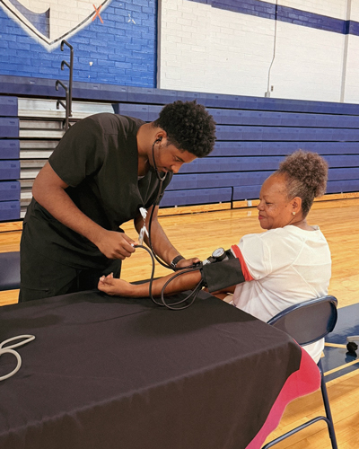Jackston Nance checking a patient's blood pressure.