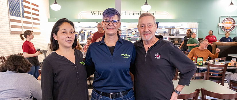 Cliff Arthur stands with two Metro Diner team members inside a busy diner dining room in Columbia, South Carolina.