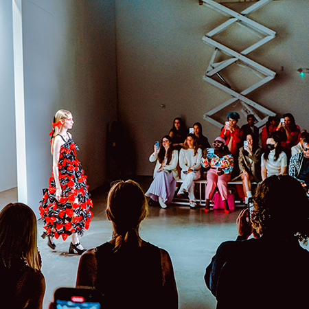 A model walks down the runway at a New York Fashion Show event and is photographed by spectators.