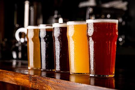 Many varieties of craft beer. Misted glass goblets with ale, lager, dark, light and unfiltered drink on wooden bar.