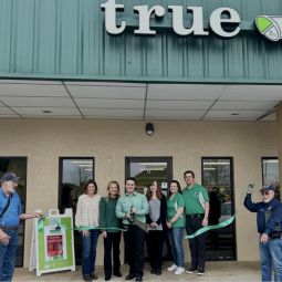 group of people cutting a ribbon in front of a pharmacy building