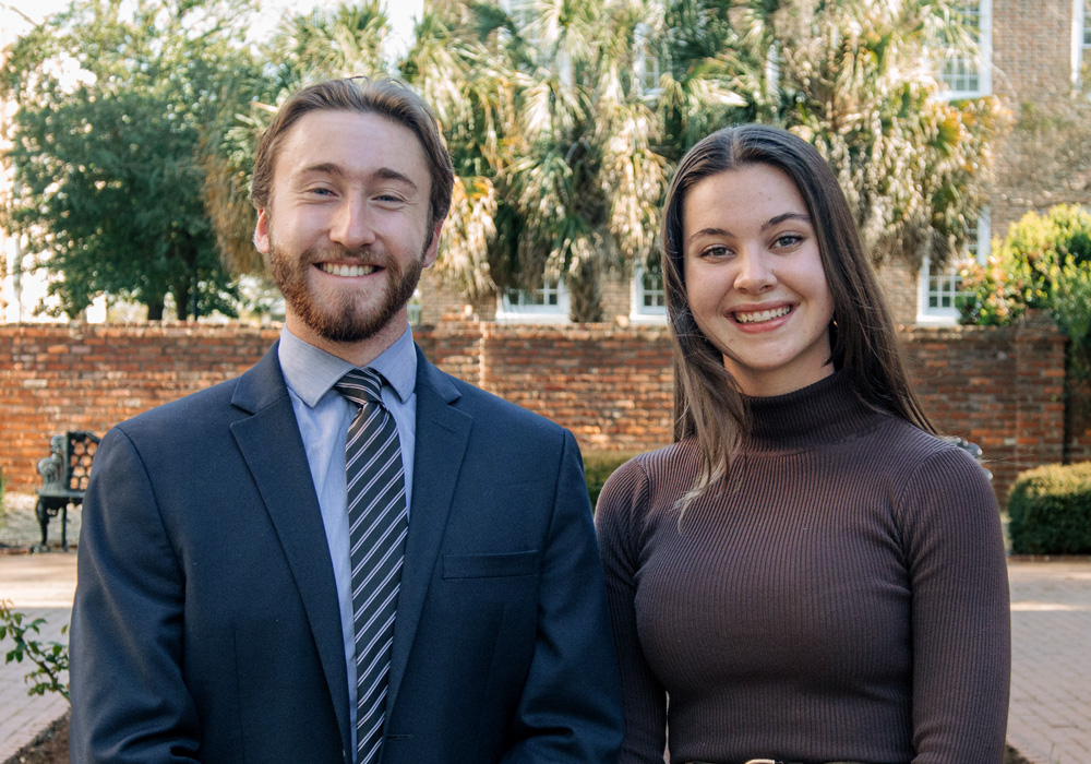 two people stand in a garden setting with a brick wall in the background