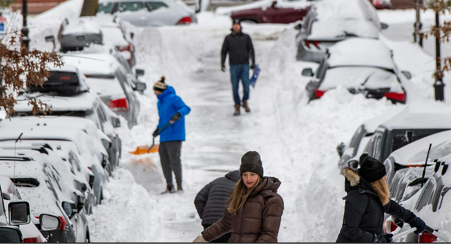 On busy snowy street, people try to dig their cars out.
