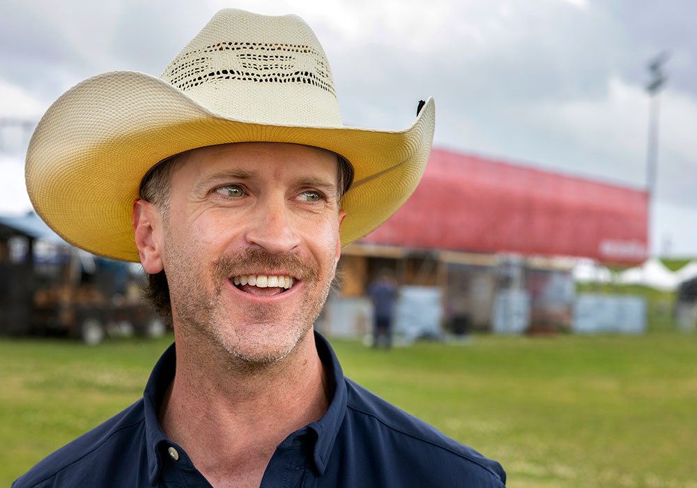 Alumnus Becker Hall smiles for the camera while wearing a straw cowboy hat.