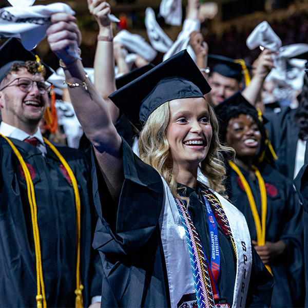Woman in cap and gown waving towel at graduation ceremony