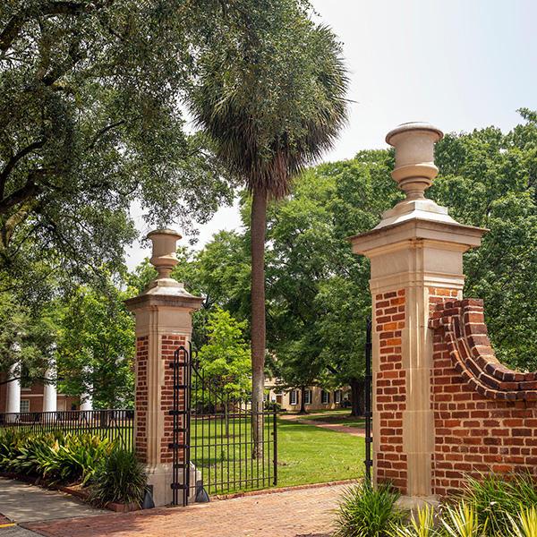 Brick and iron gate along a sidewalk and campus buildings